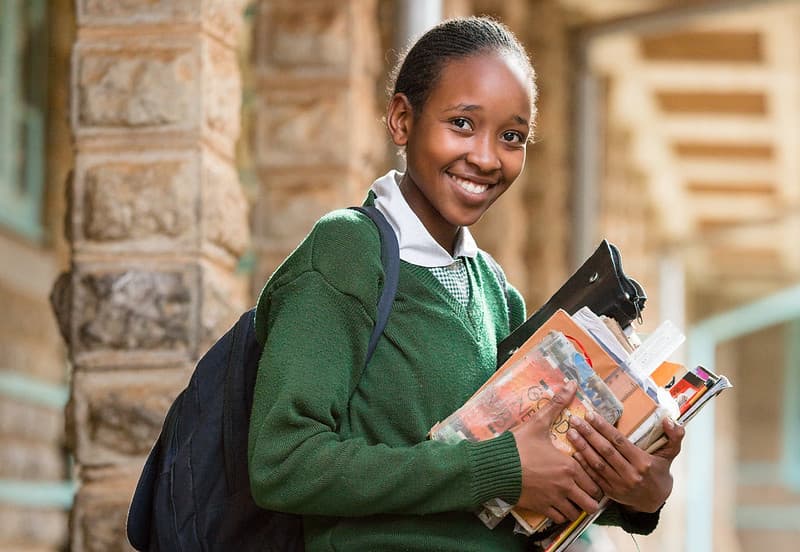 Student in green uniform smiling and holding books